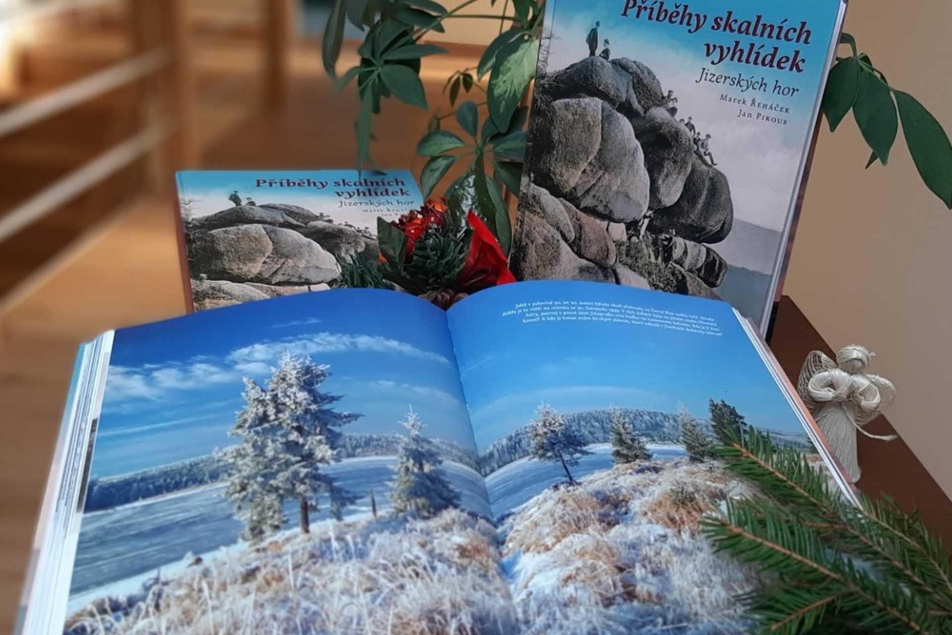 otevřená kniha Příběhy skalních vyhlídek Jizerských hor na pozadí jedné z vyhlídek se vánočními dekoracemi