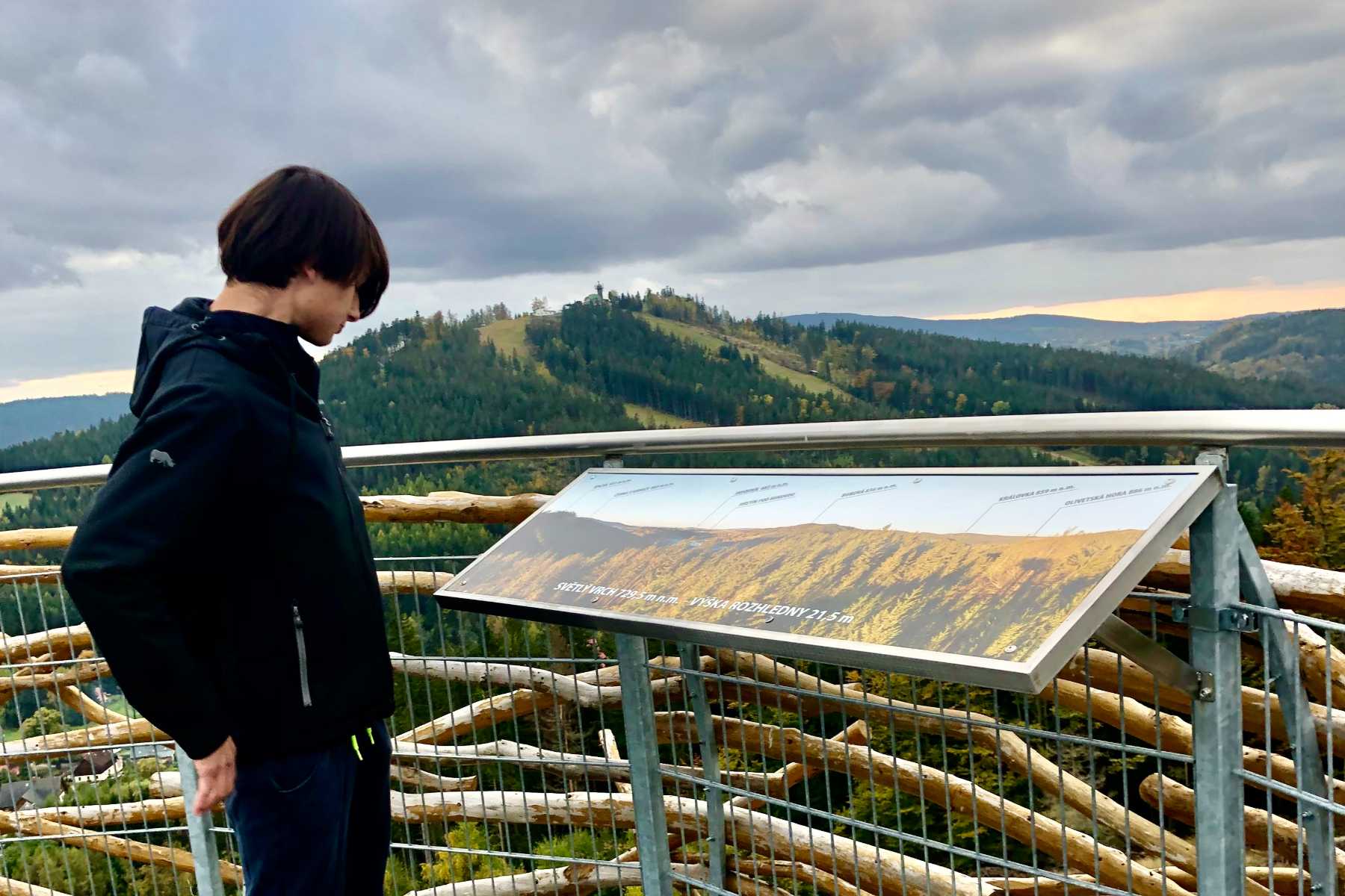 Mladý muž studující tabuli s popiskami na ochozu rozhledny Světlý vrch - Jizerské hory