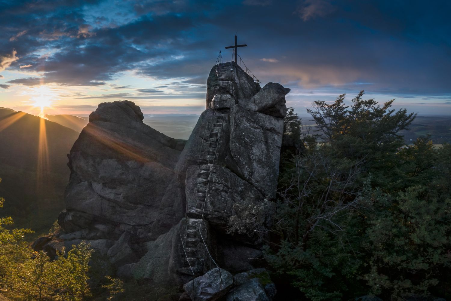 Západ slunce na vyhlídce Ořešník – skalní dominanta nad Hejnicemi, Jizerské hory. Pohled na skálu se strmými schody a křížem