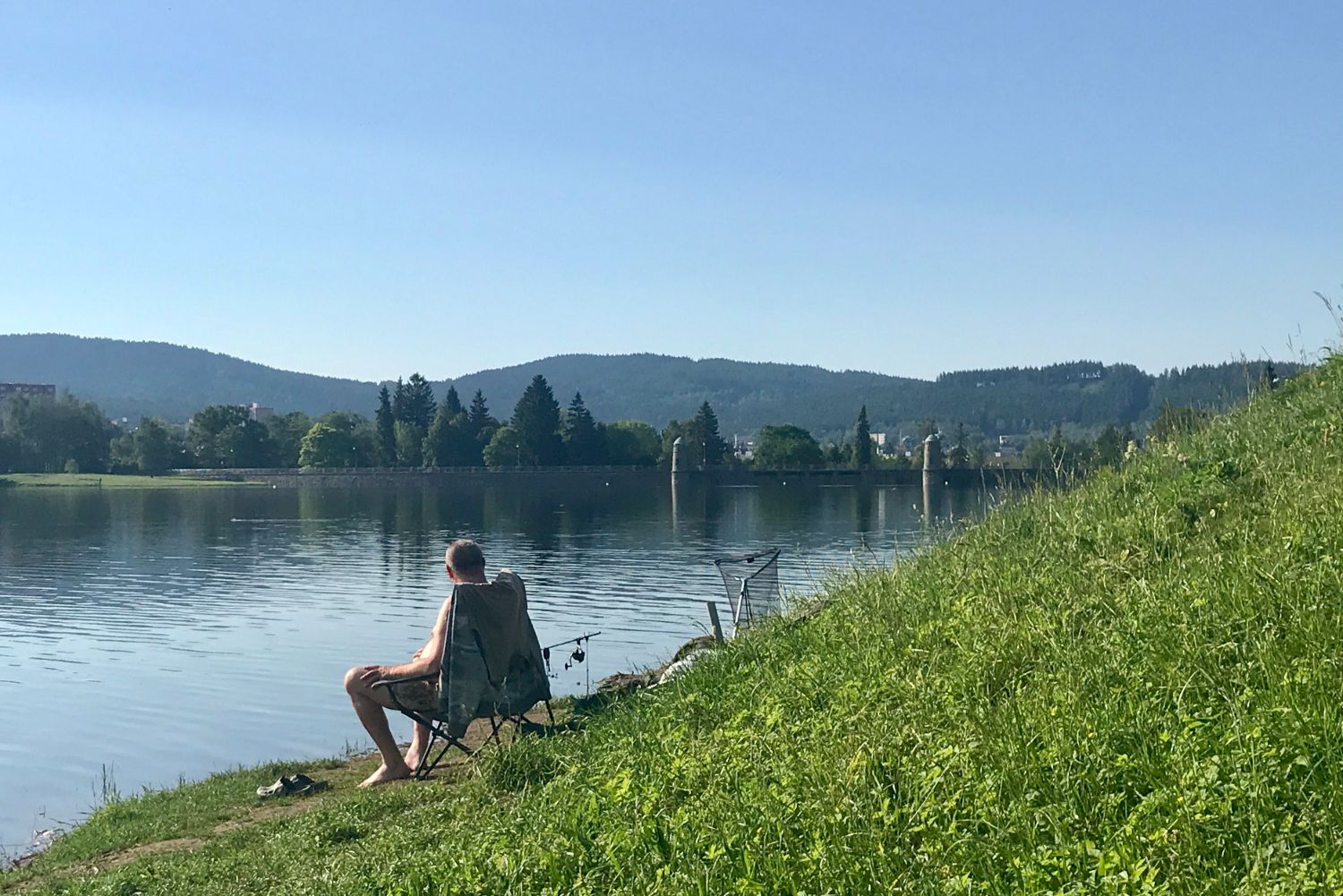 Rybář sedící zády u vody na břehu jablonecké přehrady.