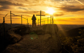 Turista na skalní vyhlídce Paličník s křížem při západu slunce – Jizerské hory