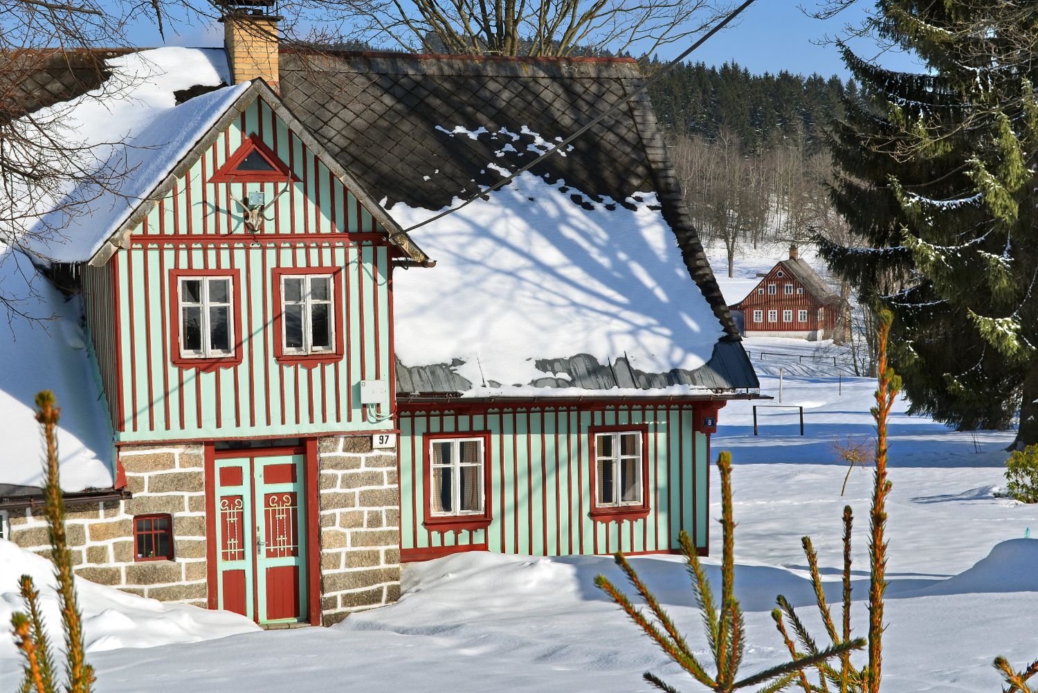 Dřevěná chalupa v Jizerských horách (Karlov) v zimě - roubení v zeleno-červeno-bílé barvě