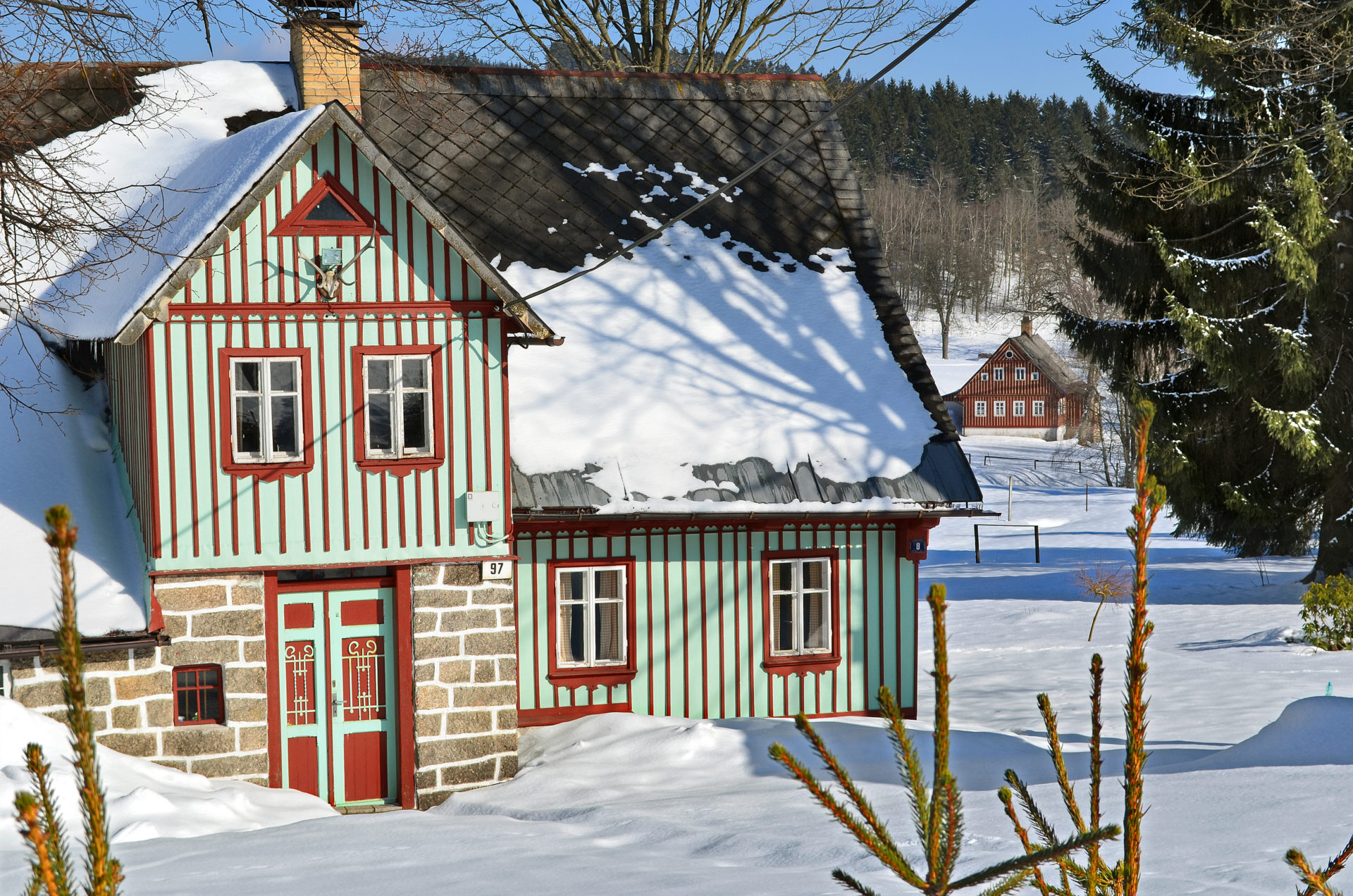 Dřevěná chalupa v Jizerských horách (Karlov) v zimě - roubení v zeleno-červeno-bílé barvě