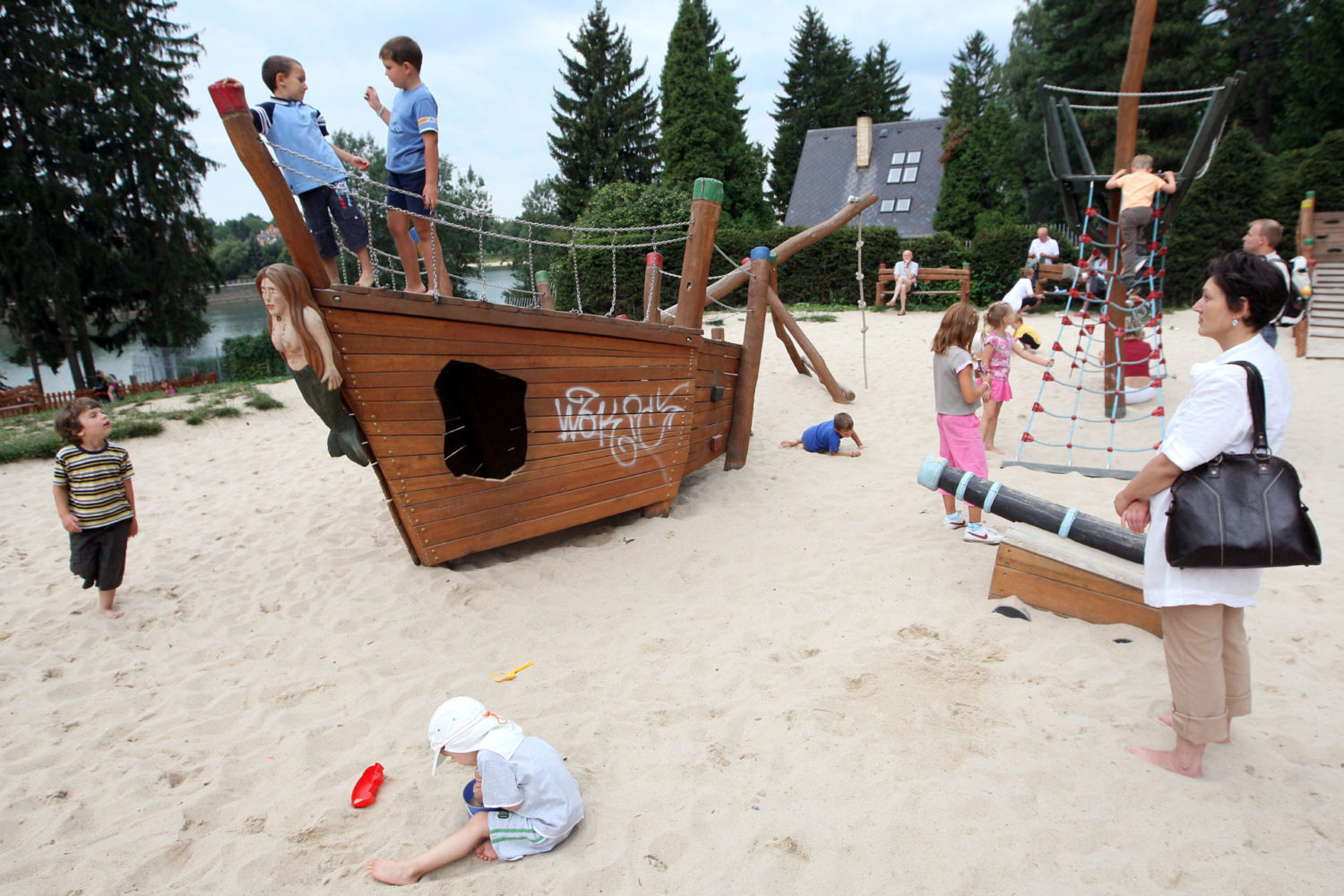 Dřevěná prolézačka ve tvaru lodě, písek a hrající si děti na dětském hřišti u přehrady v Jablonci nad Nisou - Mšeno