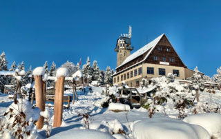 Hotel a rozhledna Královka v Jizerských horách v zimě. V popředí dětské hřiště.