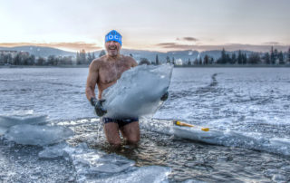 Otužilec v plavkách ve vysekané díře v ledu stojící s ledovou krou v ruce v jablonecké přehradě Mšeno