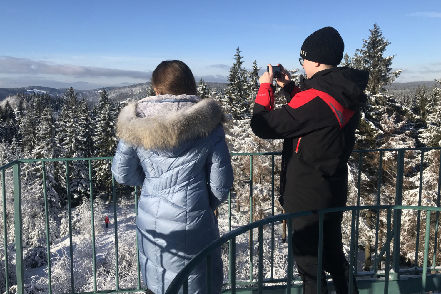 Dvojice turistů fotící si zasněženou krajinu Jizerských hor z rozhledny Slovanka